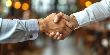 Close-up of two people shaking hands, one in a blue shirt and the other in a white shirt.