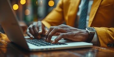 Man typing on a laptop in a yellow blazer.