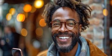 Smiling man with glasses, wearing a scarf and jacket, standing outdoors.