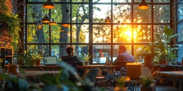 Two people work at a wooden table in a sunlit room.