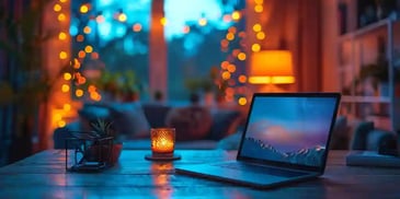 Laptop on a wooden table with a candle and small plant.