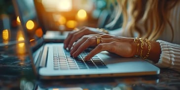 Woman typing on a laptop, wearing gold jewelry.