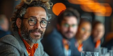 Smiling man with curly hair, glasses, and a beard in a meeting.