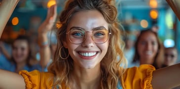 Smiling woman with glasses and hoop earrings, wearing a yellow top.